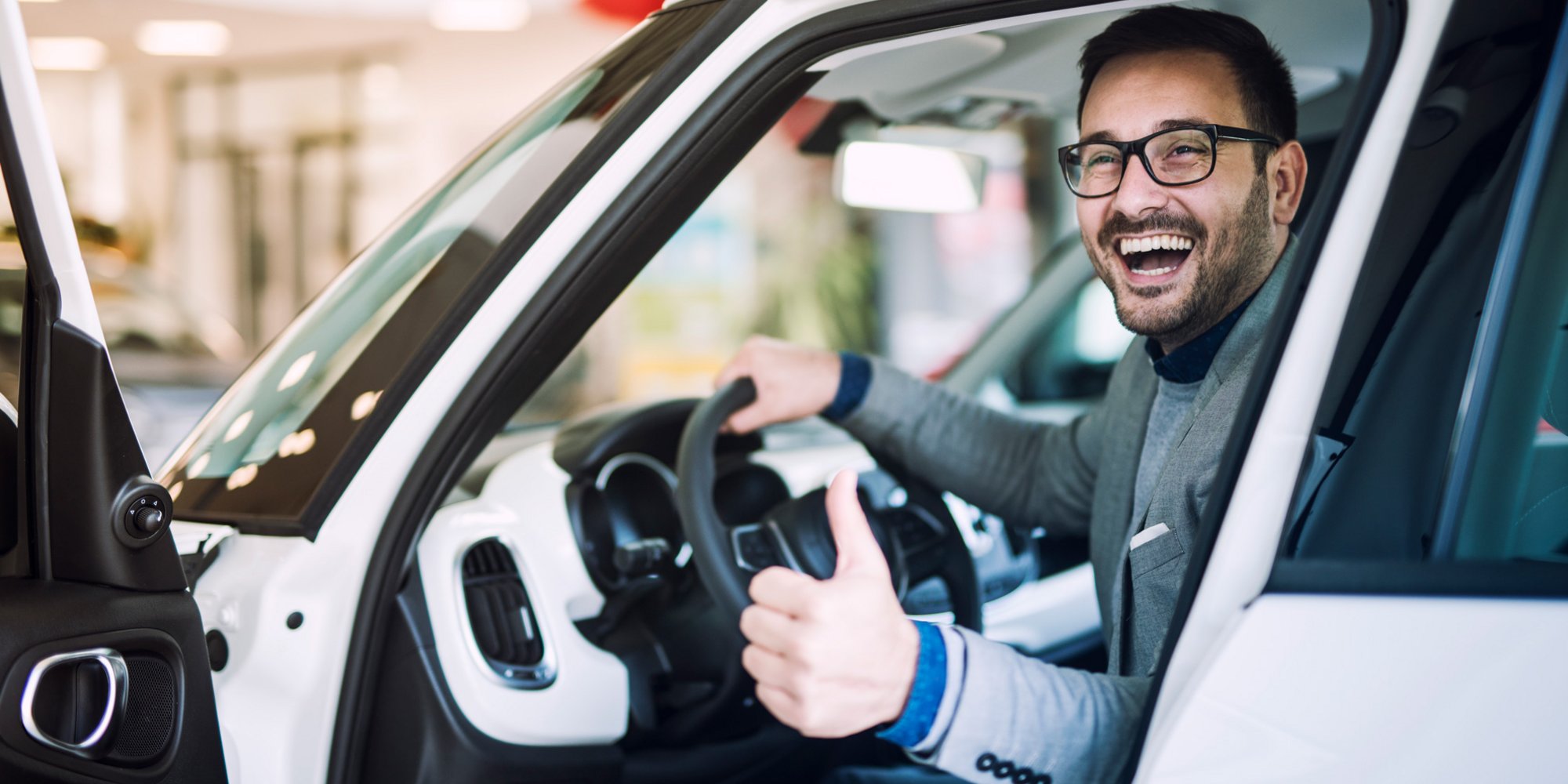 Ein lachender Mann sitzt in einem Auto und zeigt den Daumen nach oben.
